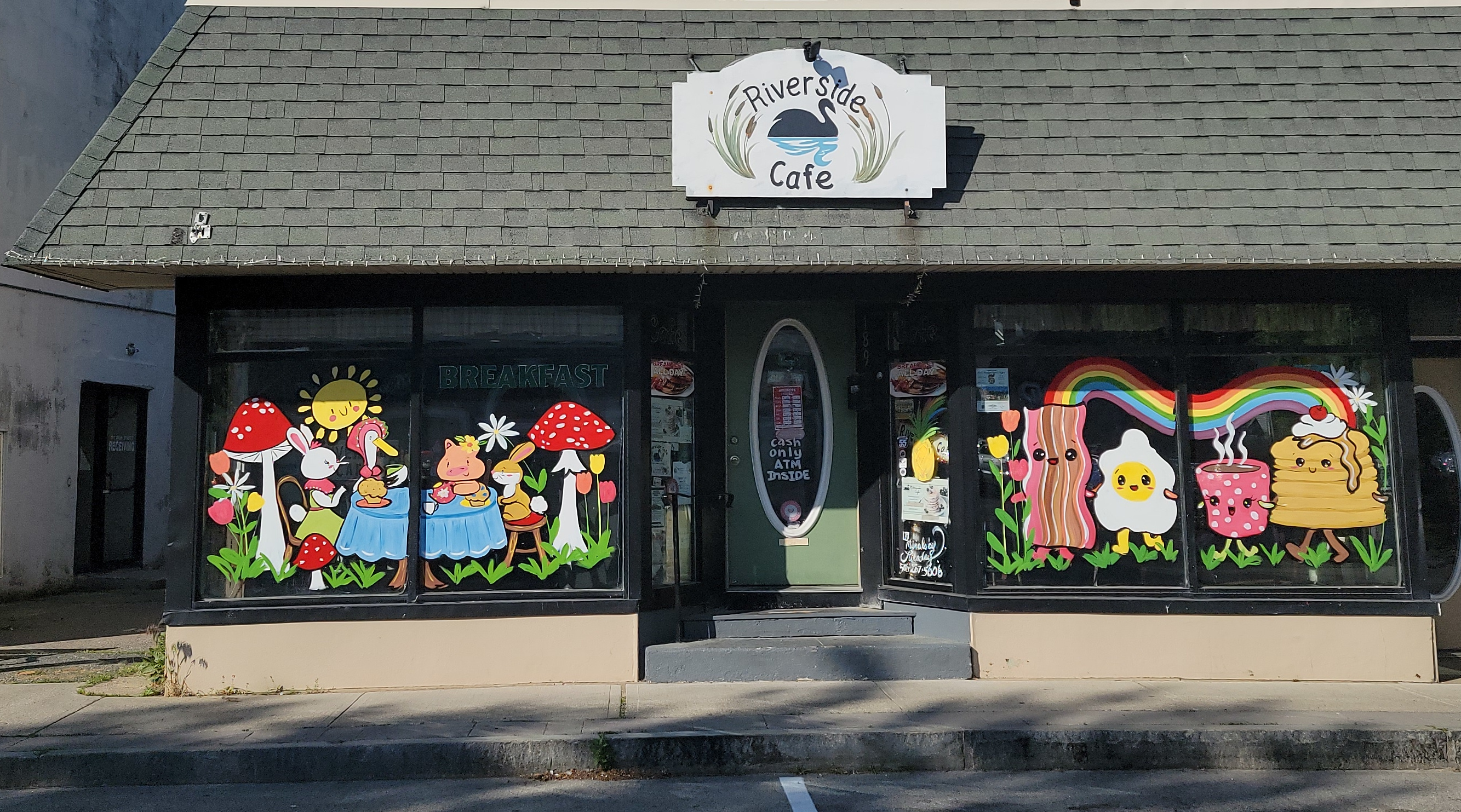 The Riverside Cafe storefront on Main Street in Wareham — swan-logo sign above the green front door, framed by hand-painted breakfast window murals
